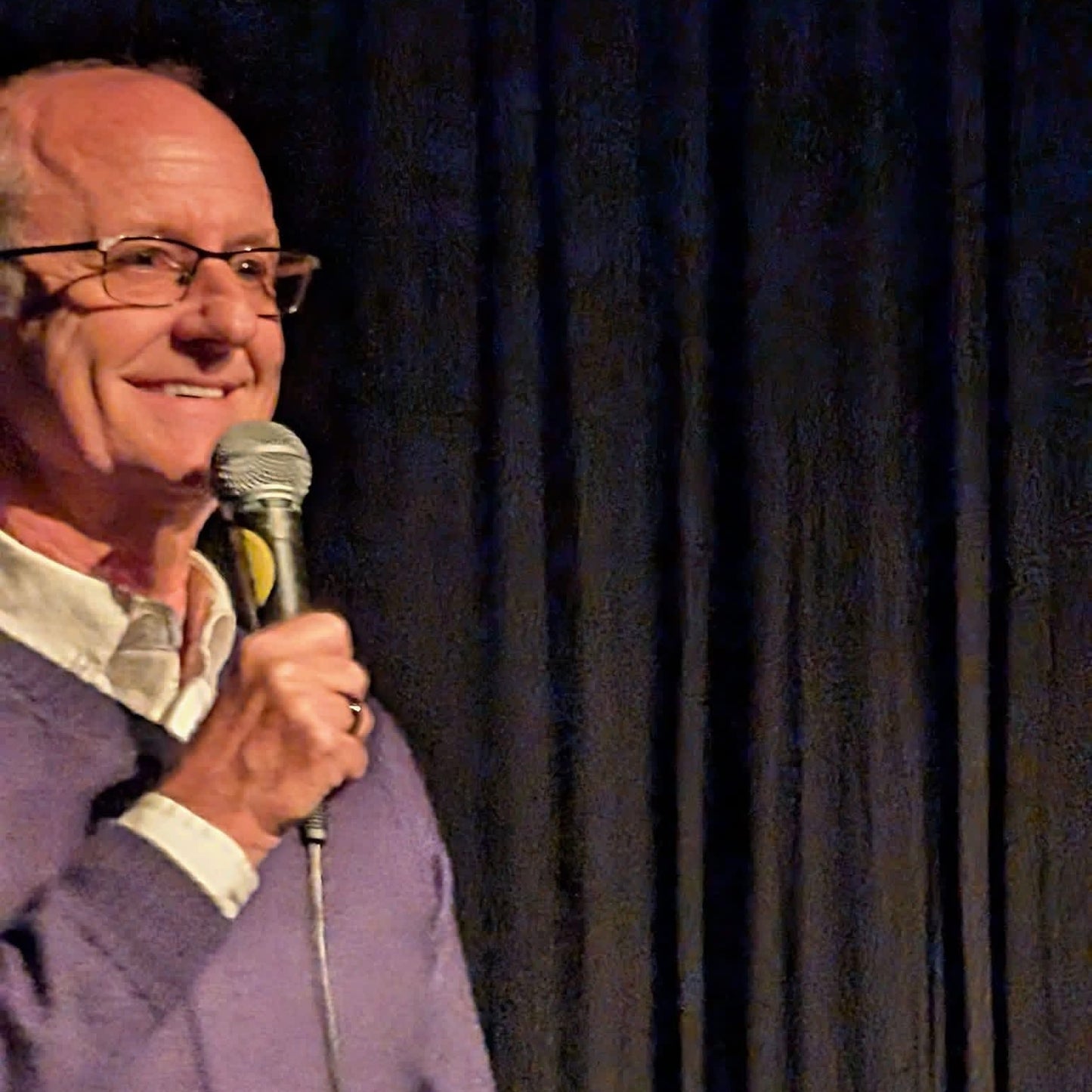 Man holding a microphone against a dark curtain background